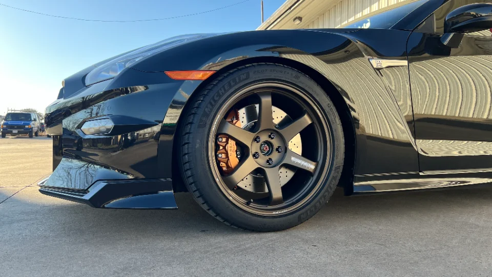 Close-up of a black Nissan GT-R's front wheel, featuring Volk TE37 wheels, Michelin tires, and bronze Brembo calipers.