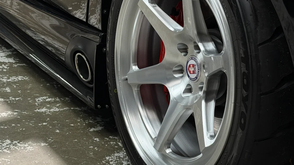 Close-up of a car's silver HPE Performance wheels, red brake calipers, Toyo tires, and carbon fiber side skirt with a side exit exhaust.