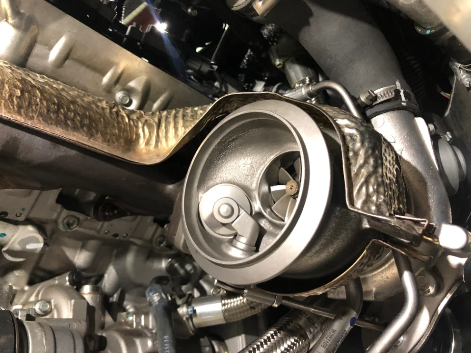 Close-up view of a turbocharger with its heat shield and exhaust manifold in a car's engine bay.