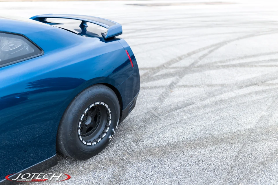 Rear view of a blue Nissan GT-R with drag slicks and a spoiler on a track with tire marks.