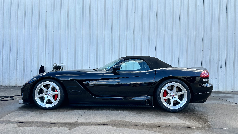 Black Dodge Viper convertible with aftermarket silver wheels and red brake calipers parked next to a metal building.