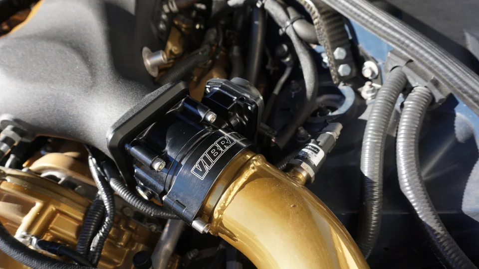 Close-up of a custom gold intake pipe with a black Vibrant Performance blow-off valve in a high-performance engine bay.