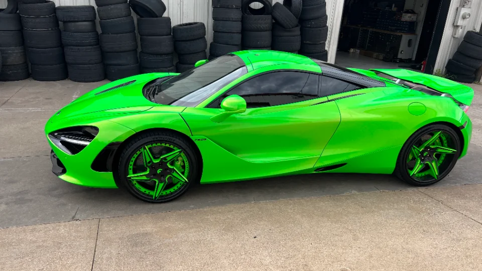 A bright green McLaren 720S with custom green and black wheels parked outside a shop with stacks of tires.