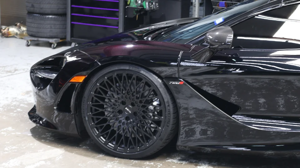 A black McLaren 720S with aftermarket multi-spoke wheels parked inside a performance tuning shop.