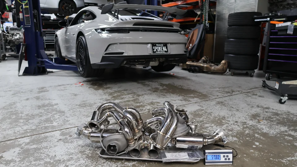 Porsche 911 GT3 on a lift in a performance shop with a high-performance turbo exhaust system on a scale on the floor