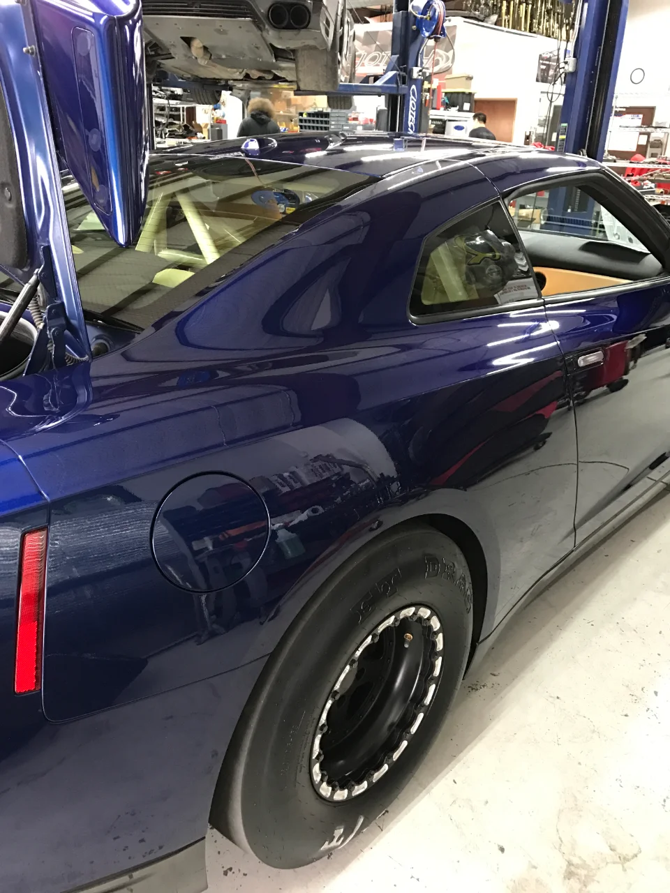 A blue Nissan GT-R with drag slicks and beadlock wheels in a performance tuning shop.