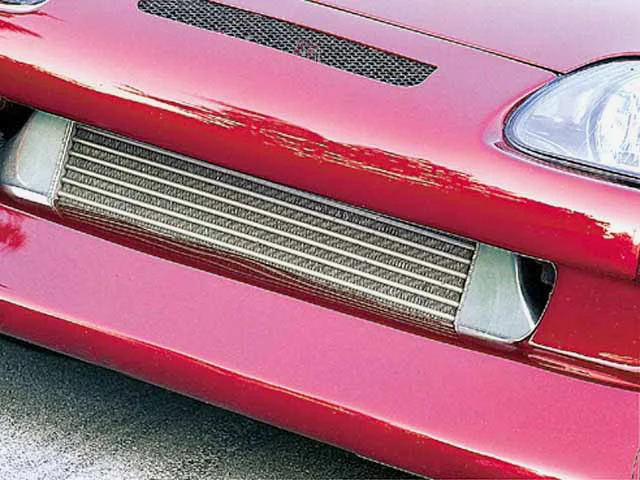 Close-up of a front-mounted intercooler visible through the bumper of a red performance car.