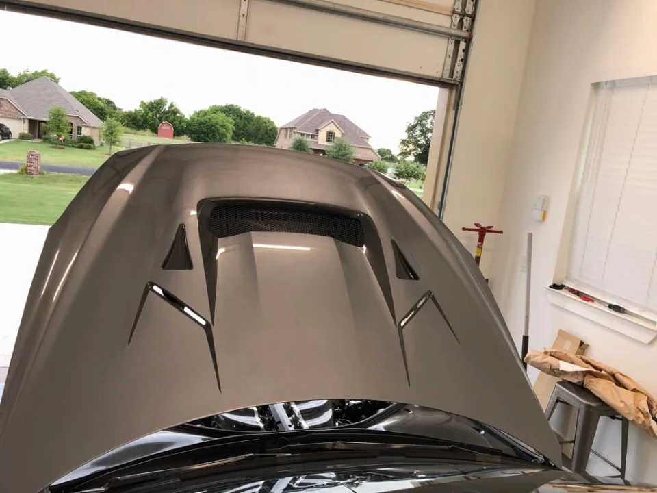 Close-up of a vented carbon fiber hood on a performance car in a garage setting.