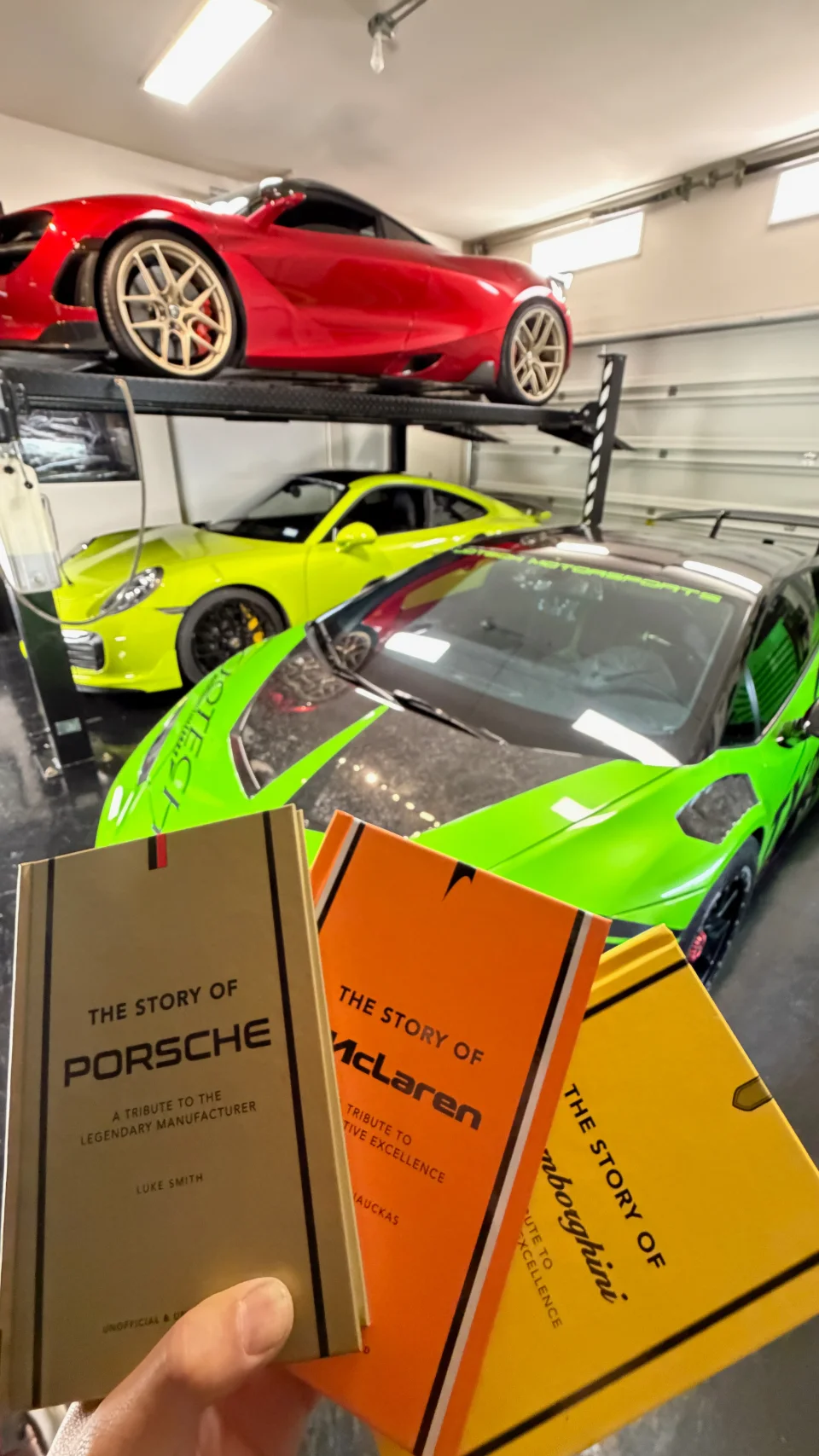 A Jotech garage with a red sports car on a lift and a green Lamborghini, with books about Lamborghini, McLaren, and Porsche.