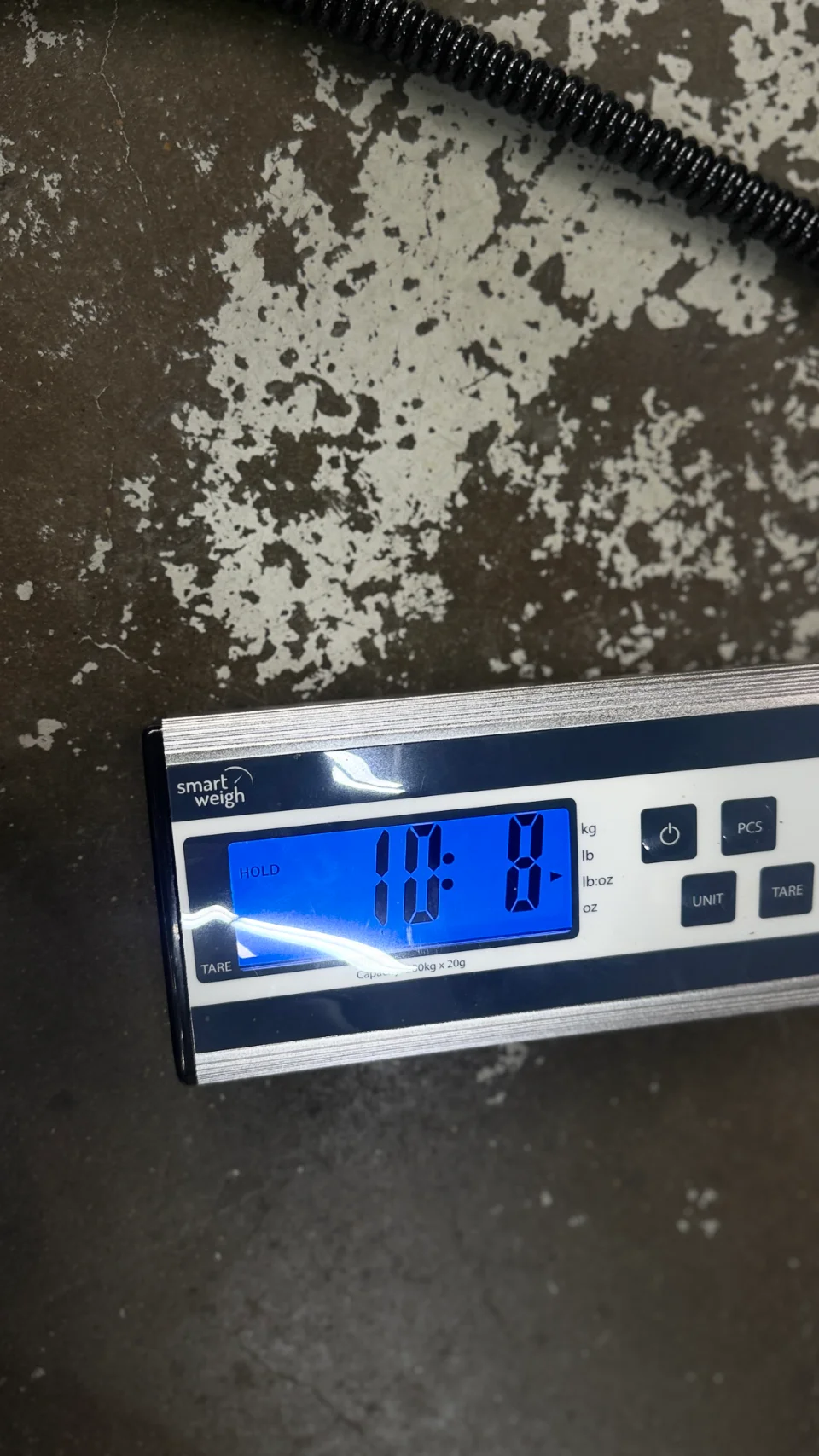 A Smart Weigh digital scale displaying a measurement of 11.8 on a blue backlit screen, resting on a concrete floor.