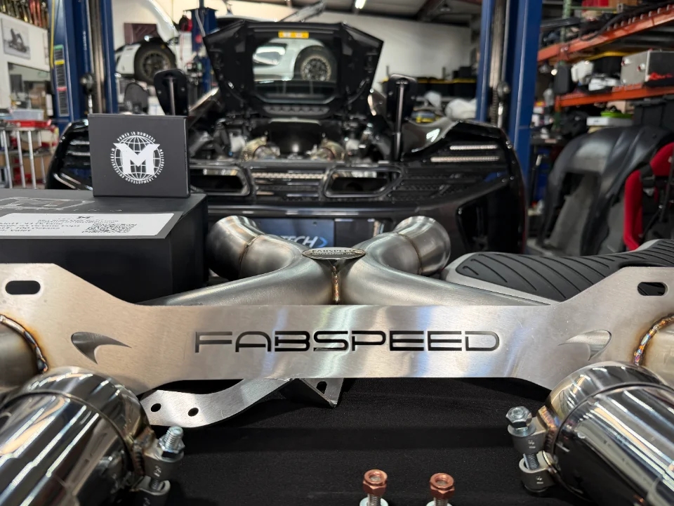 Fabspeed exhaust system for a McLaren supercar, displayed in a performance tuning shop with the car on a lift.