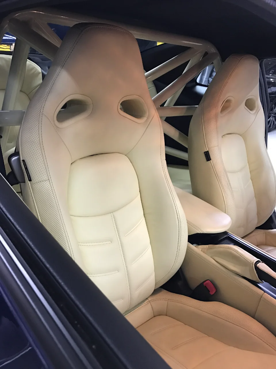 Close-up of a car's interior featuring cream-colored racing seats and a white roll cage.
