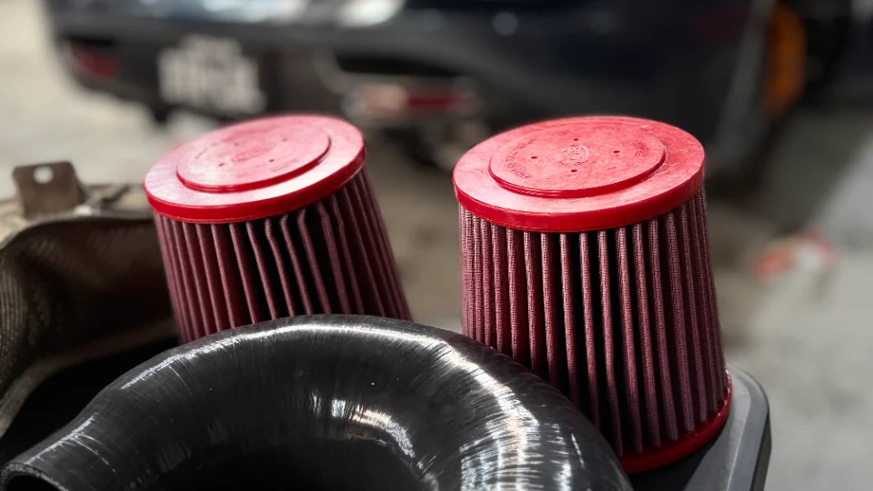 Close-up of two red performance air filters and a black silicone intake hose, likely for a car's induction system.