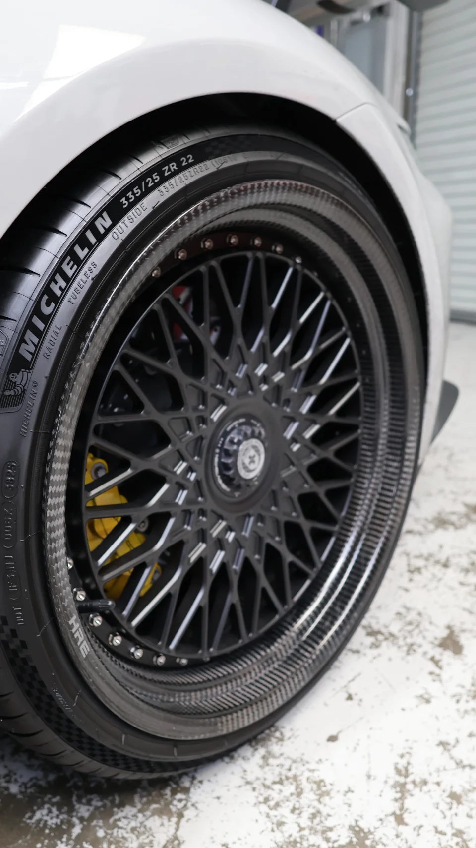 A close-up detail shot of a white car's carbon fiber HRE wheel with Michelin tire and yellow brake caliper.