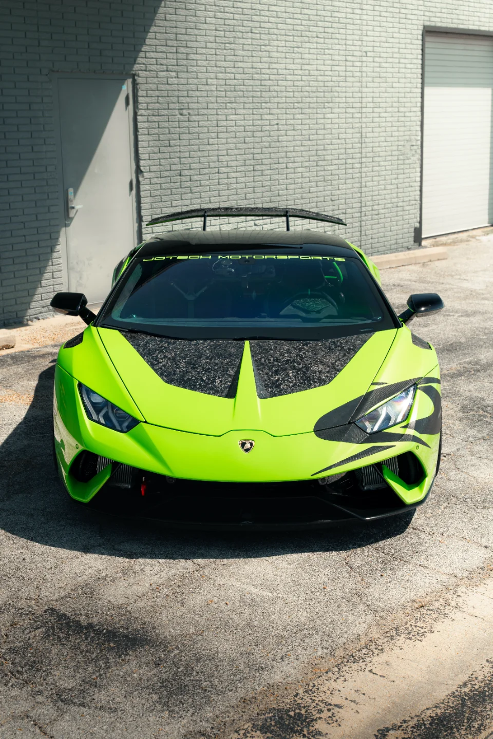 A lime green Lamborghini Huracan with a carbon fiber hood and Jotech Motorsports branding parked in front of a shop.