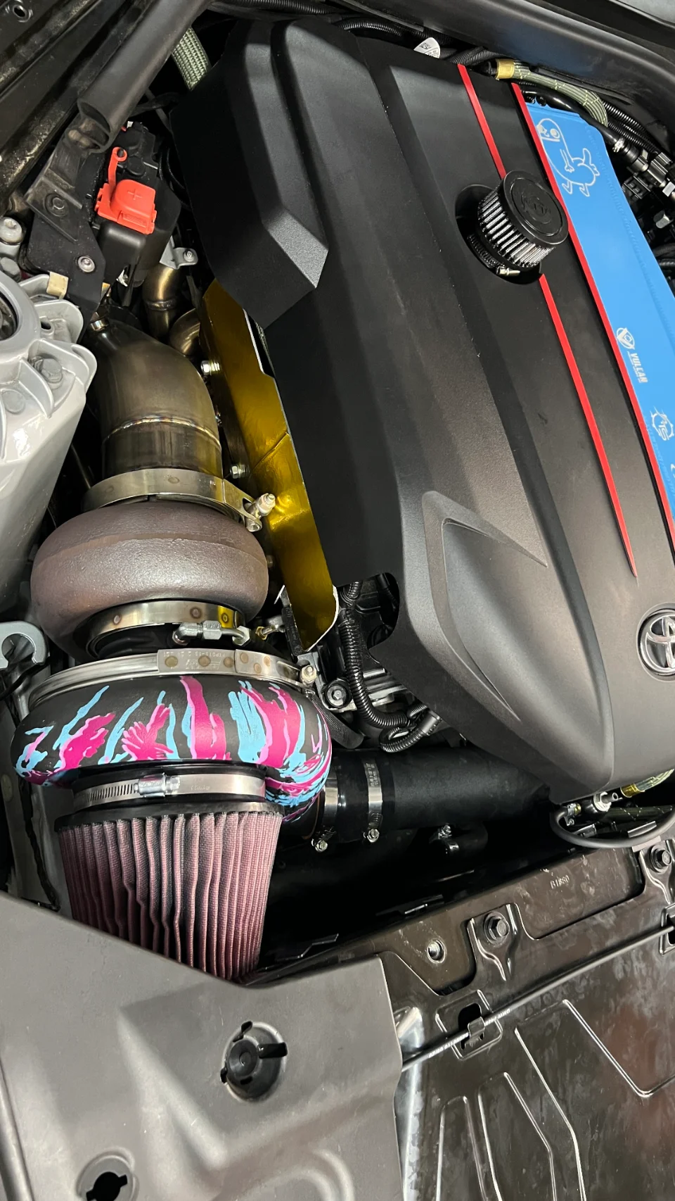 Close-up view of a modified Toyota Supra engine bay featuring a large aftermarket turbocharger and air intake.
