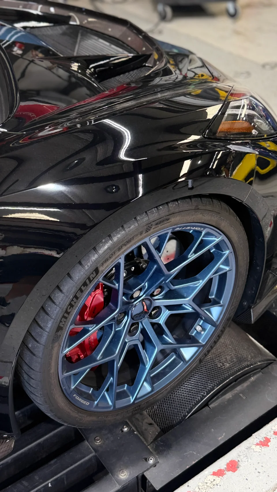 Black C8 Corvette on a dyno with blue aftermarket wheels and red brake calipers, showcasing performance tuning.