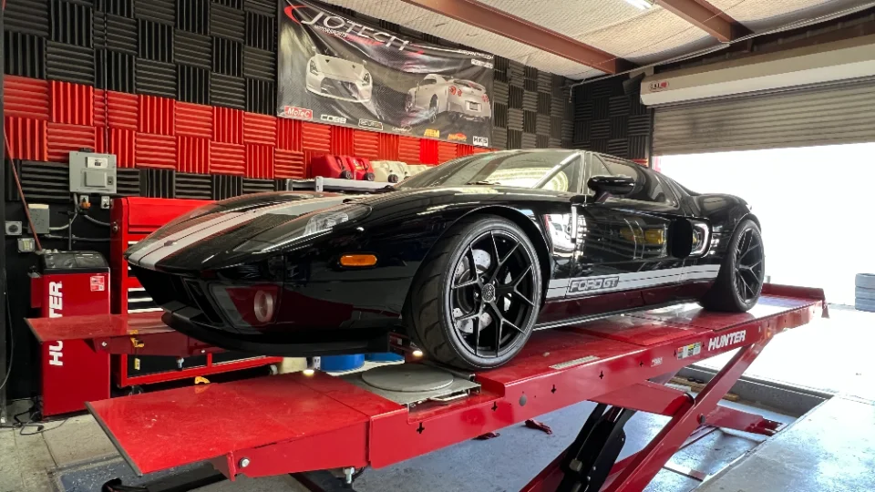 Black Ford GT with white racing stripes on a red dyno lift in a Jotech Motorsports performance shop.
