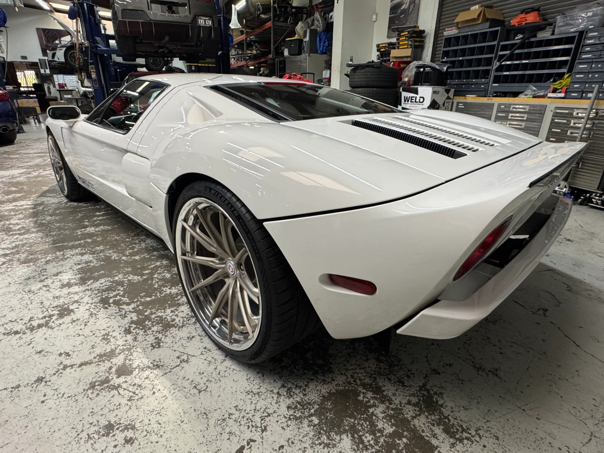 A white Ford GT supercar with custom HRE wheels parked inside a performance tuning shop.