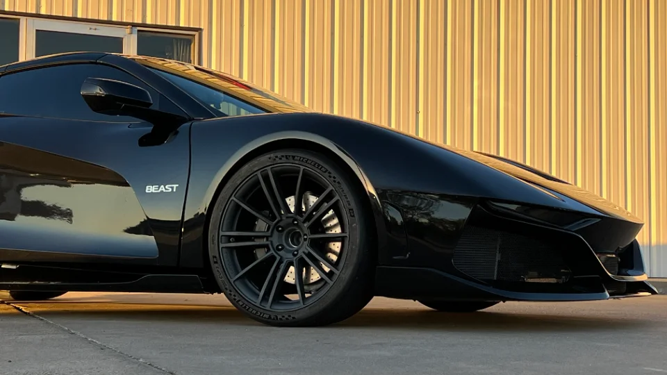 A sleek black McLaren sports car with custom black multi-spoke wheels parked in front of a corrugated metal building.
