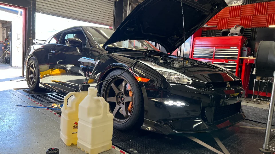 Black Nissan GT-R on a dynamometer at a performance tuning shop with the hood open.