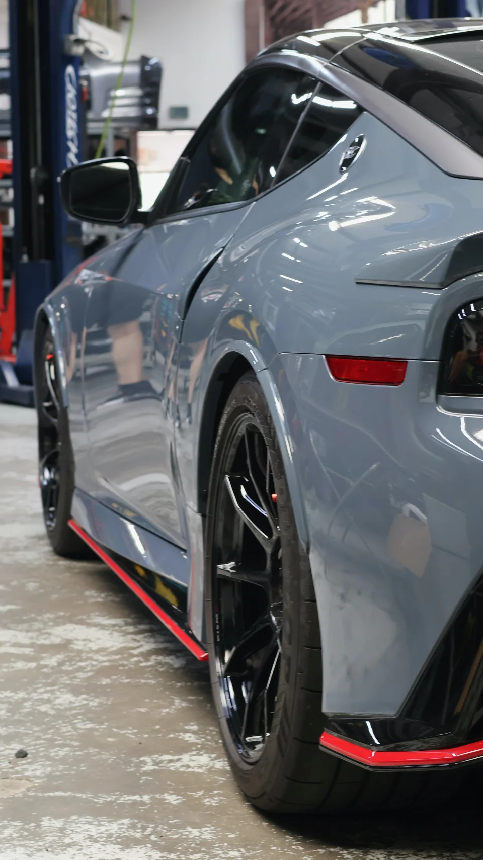 A grey Nissan Z with aftermarket wheels and red aero accents parked in a performance shop, viewed from the rear quarter.