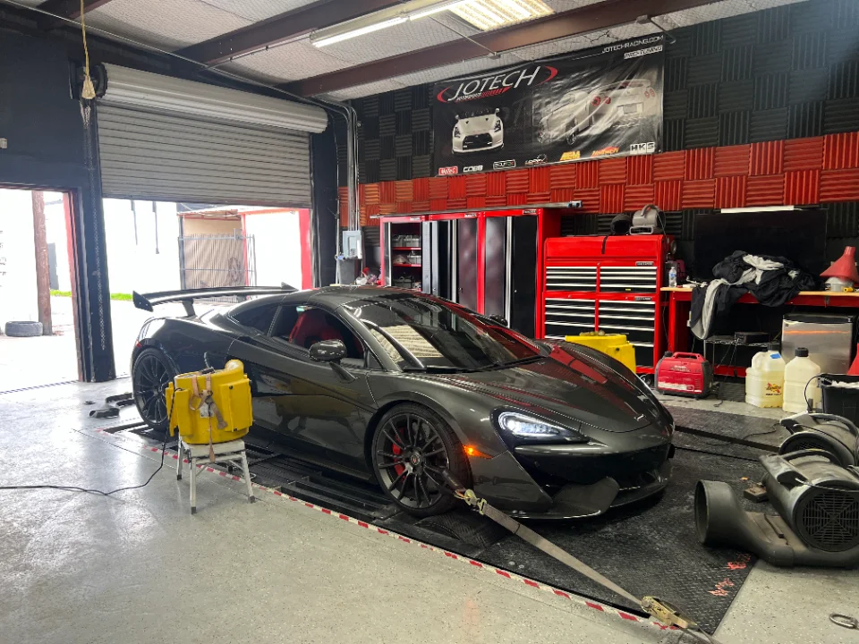 A grey McLaren sports car is strapped to a dynamometer inside the Jotech Motorsports tuning shop.