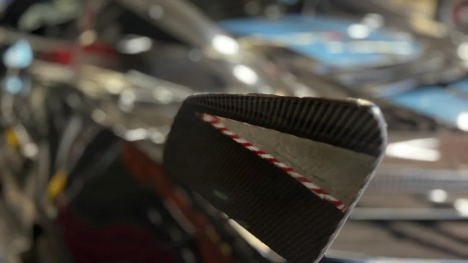 Close-up detail of a carbon fiber car part with a red and white striped edge, likely an exterior aerodynamic component.