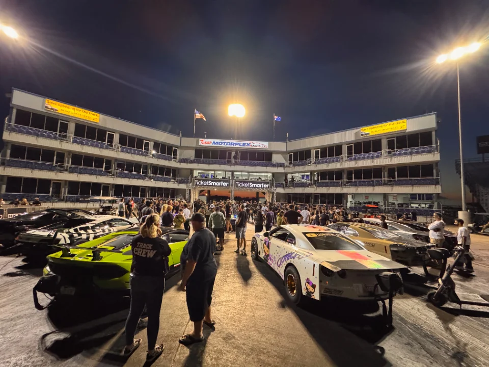 High-horsepower race cars, including a lime green Lamborghini and a white Nissan GT-R, in the staging lanes at Texas Motorplex during a night event.