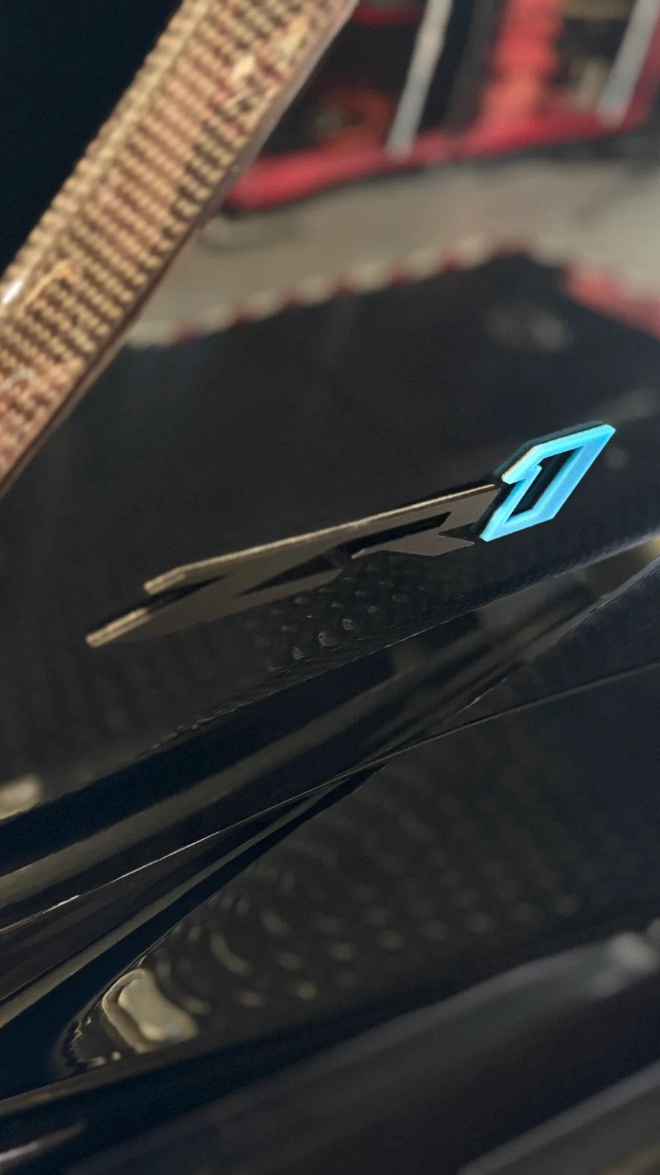 Close-up detail of a Jotech badge with a glowing blue 'J' on a carbon fiber car panel, showcasing the brand's emblem.