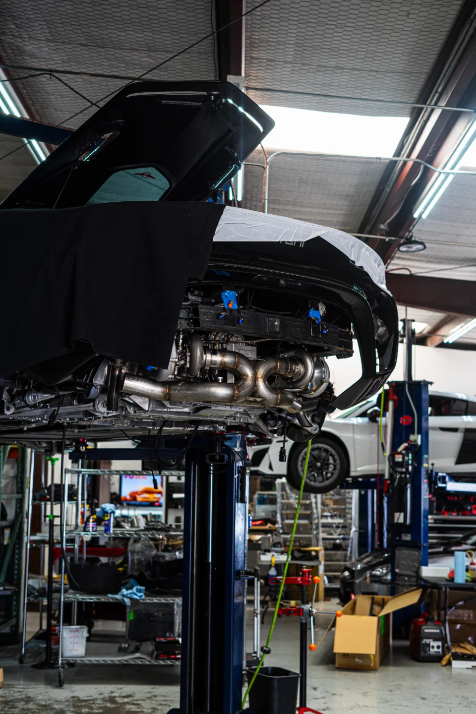A McLaren supercar on a lift in a performance shop, with its rear bumper removed to reveal twin turbochargers and custom exhaust system.
