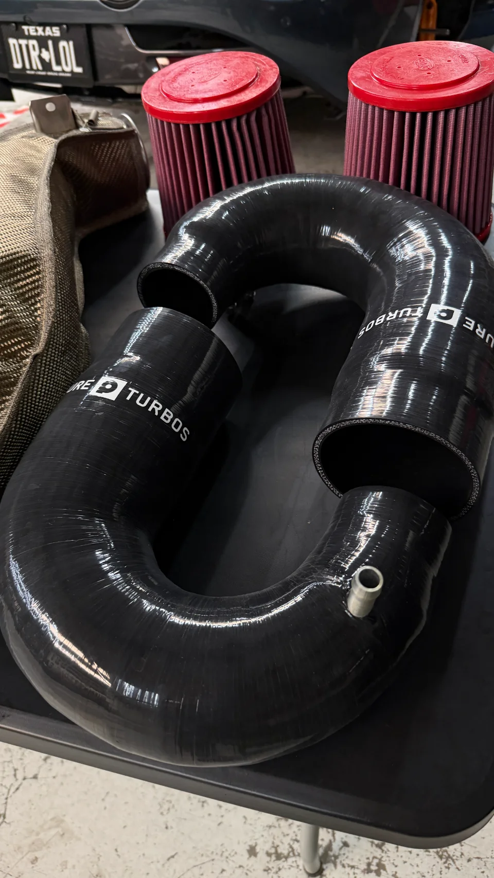 Pure Turbos silicone intake pipes and red air filters for a performance vehicle upgrade, laid out in a shop.
