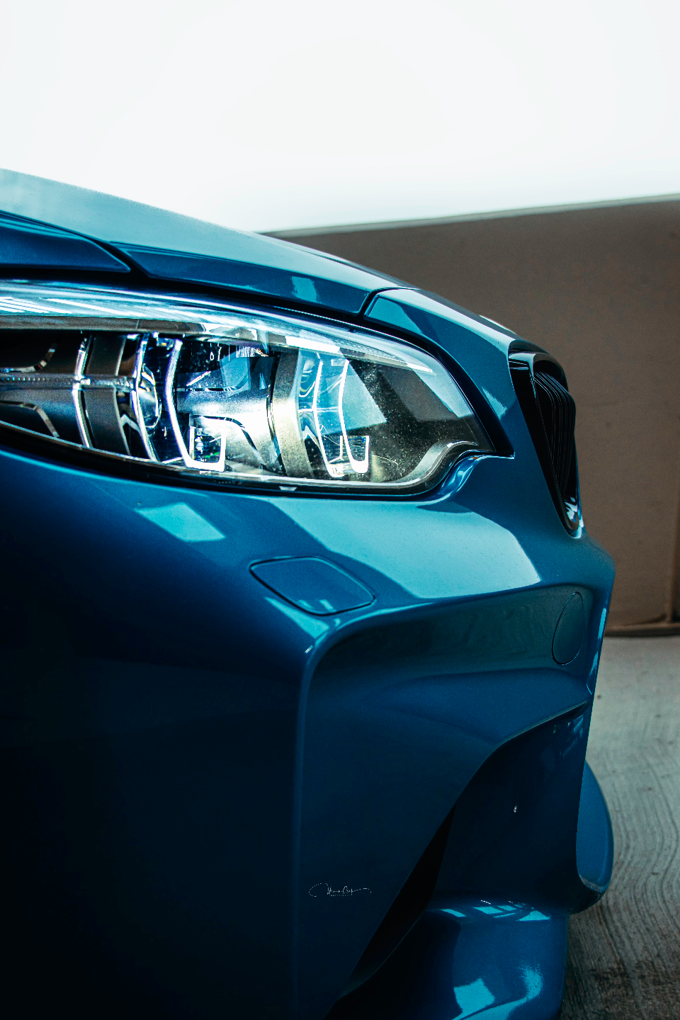 A close-up detail shot of the bright blue BMW M2 front bumper and LED headlight, showcasing the car's design.