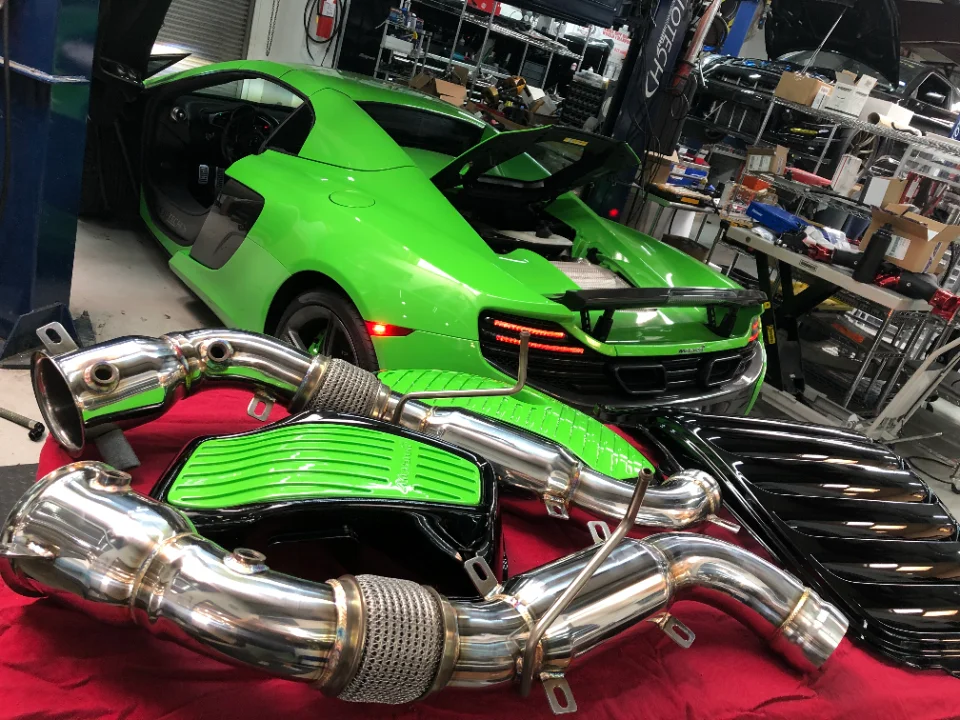 Aftermarket exhaust components laid out in front of a bright green McLaren supercar in a performance tuning shop.