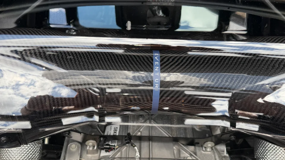 Close-up of a carbon fiber Eventuri intake system in a car's engine bay, showcasing the weave and branding.