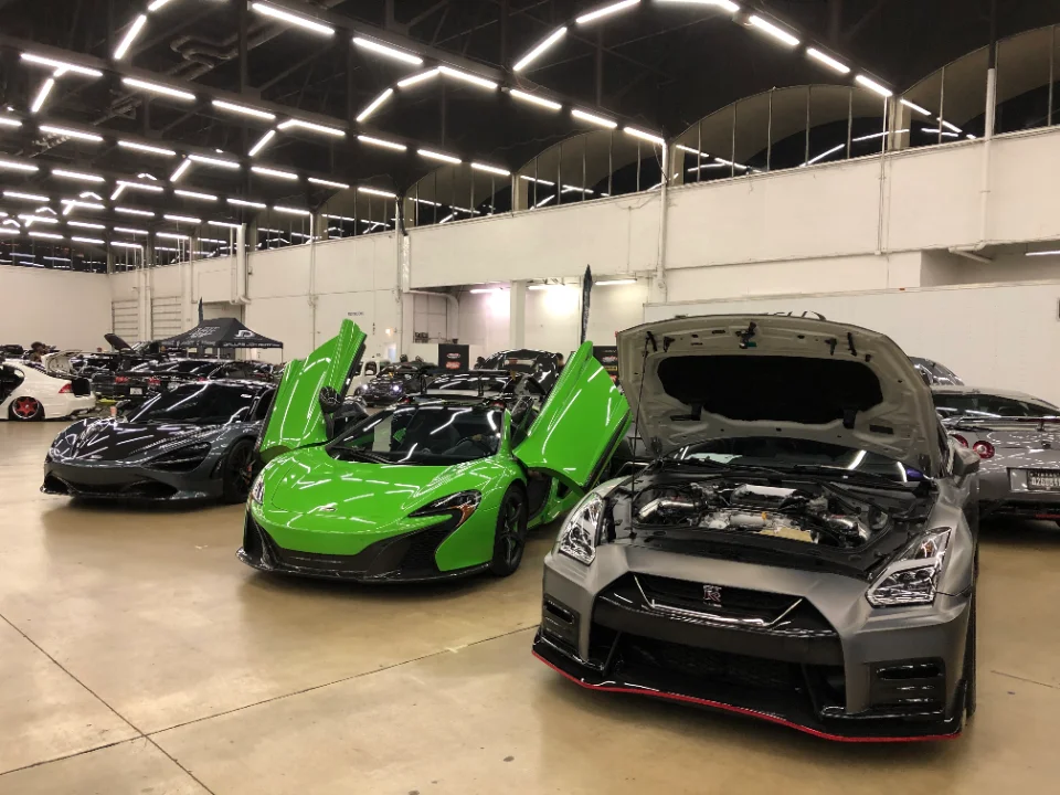 A grey Nissan GT-R with its hood open and a green McLaren with doors up at an indoor car show.