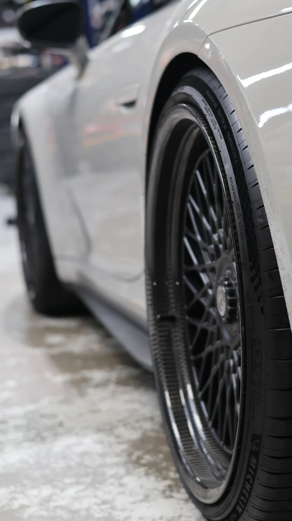 Close-up detail of a white Porsche's wheel and Michelin tire, showcasing the intricate spoke design and carbon fiber rim.