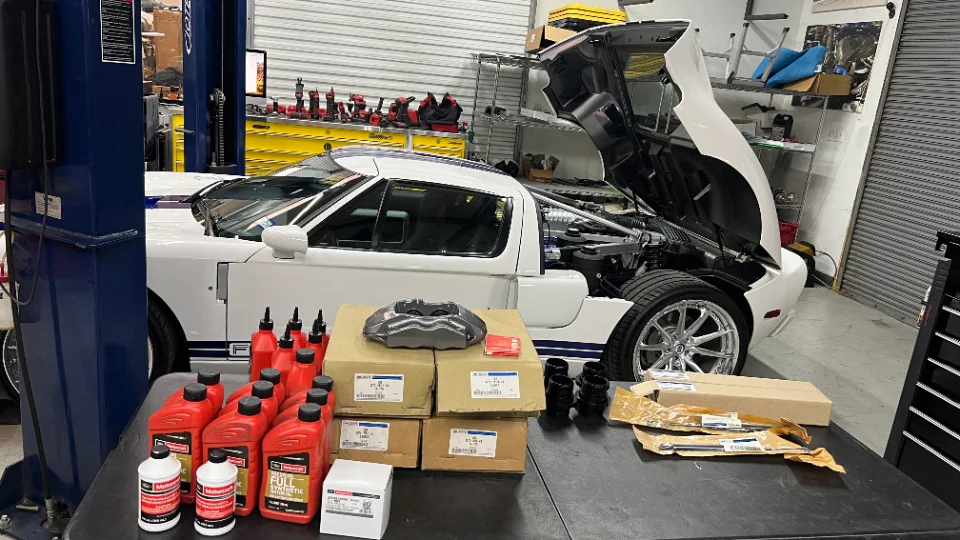 White Ford GT on a lift in a Jotech Motorsports shop with new brake calipers, oil, and other parts on a table.
