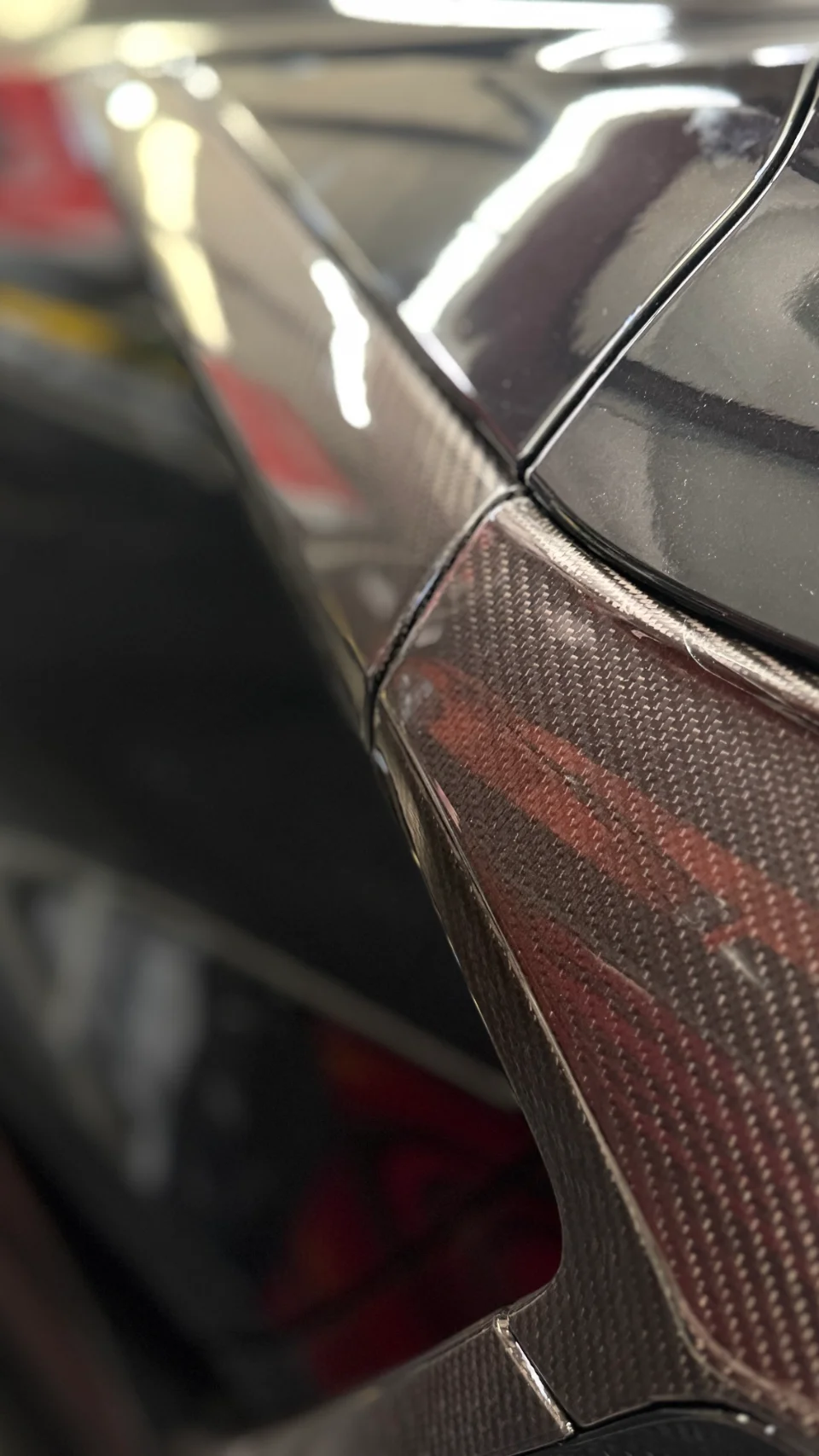 Close-up of a car's carbon fiber body panel, showcasing the weave and glossy finish.
