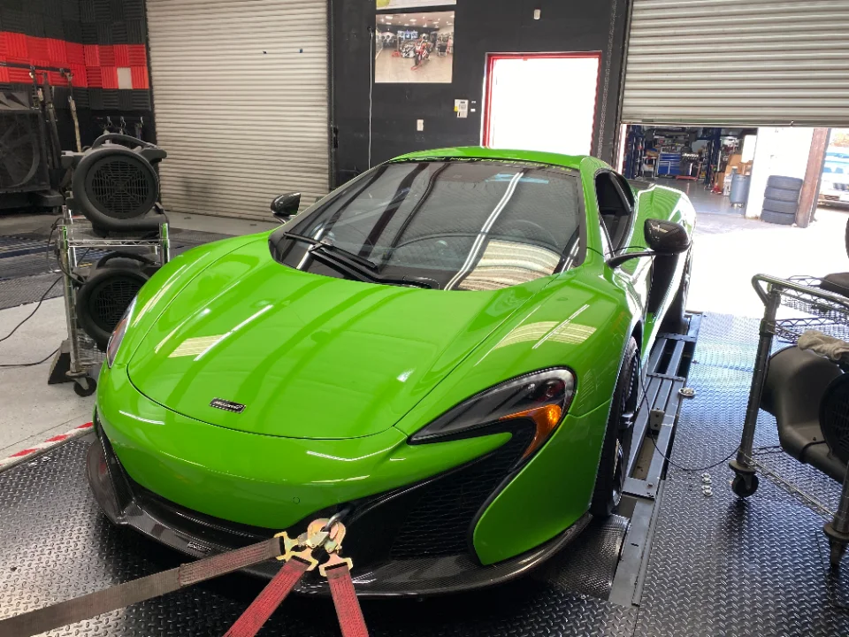 A bright green McLaren supercar is strapped down on a dynamometer in a performance tuning shop, with large fans positioned in front.