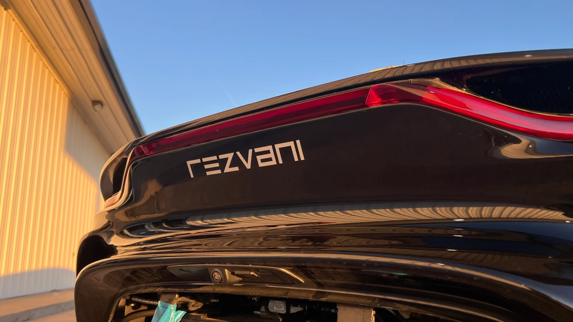 Close-up of the rear of a black Rezvani car, showing the taillight and Rezvani badge under golden hour light.