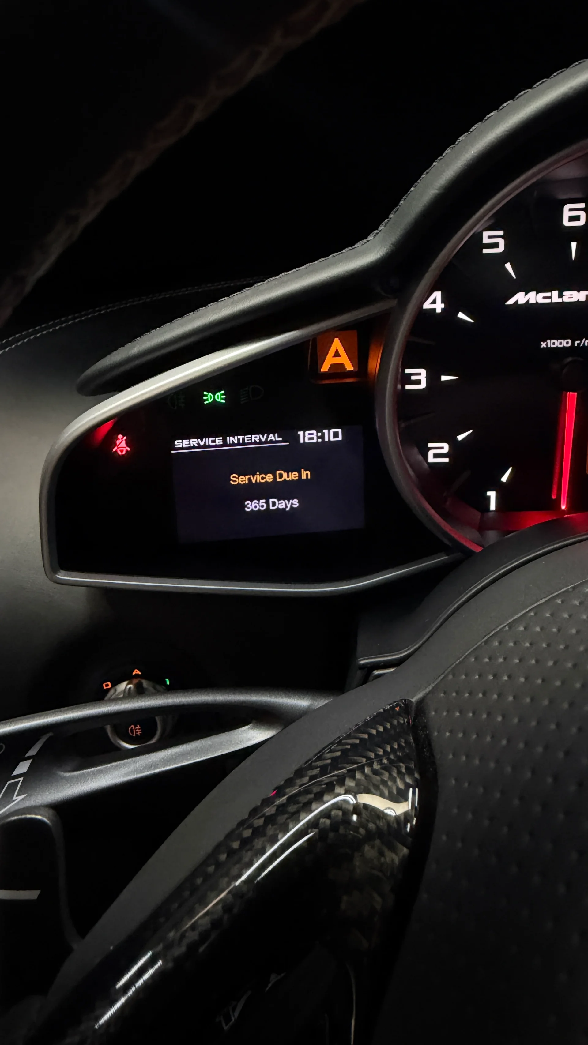 McLaren dashboard showing a 'Service Due In 365 Days' message on the digital display and a carbon fiber steering wheel.