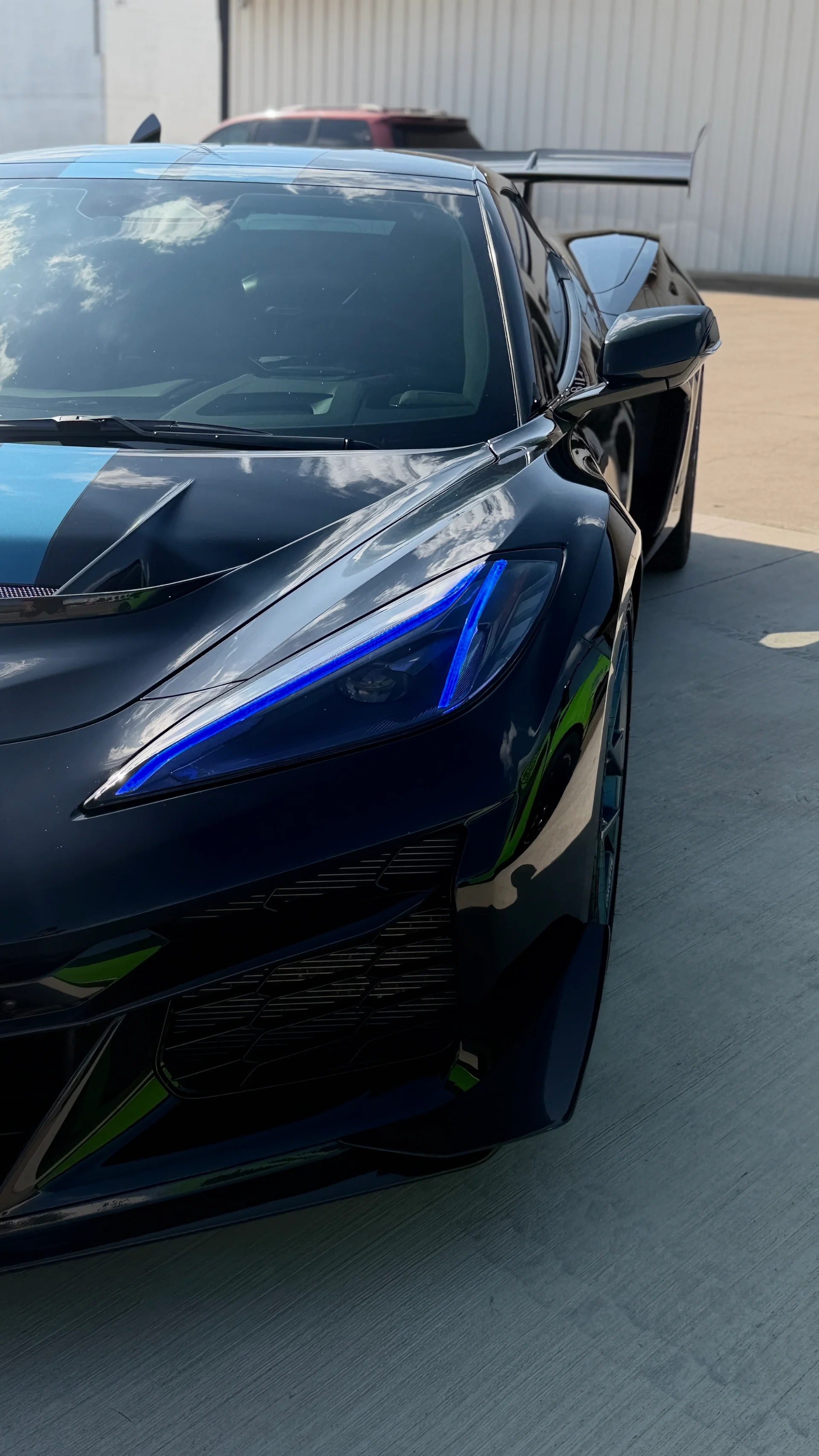 A black Chevrolet Corvette C8 with blue racing stripes and illuminated blue headlights, parked outdoors.