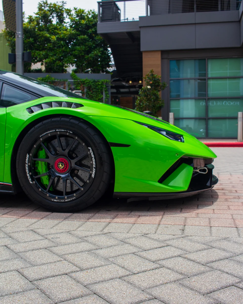 Close-up of a bright green Lamborghini Huracan with Forgeline wheels and carbon ceramic brakes parked on a paved street.