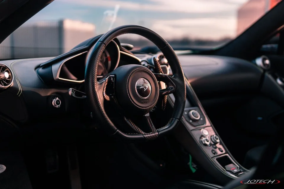 A close-up detail shot of the McLaren's interior, featuring the steering wheel with carbon fiber accents and dashboard.
