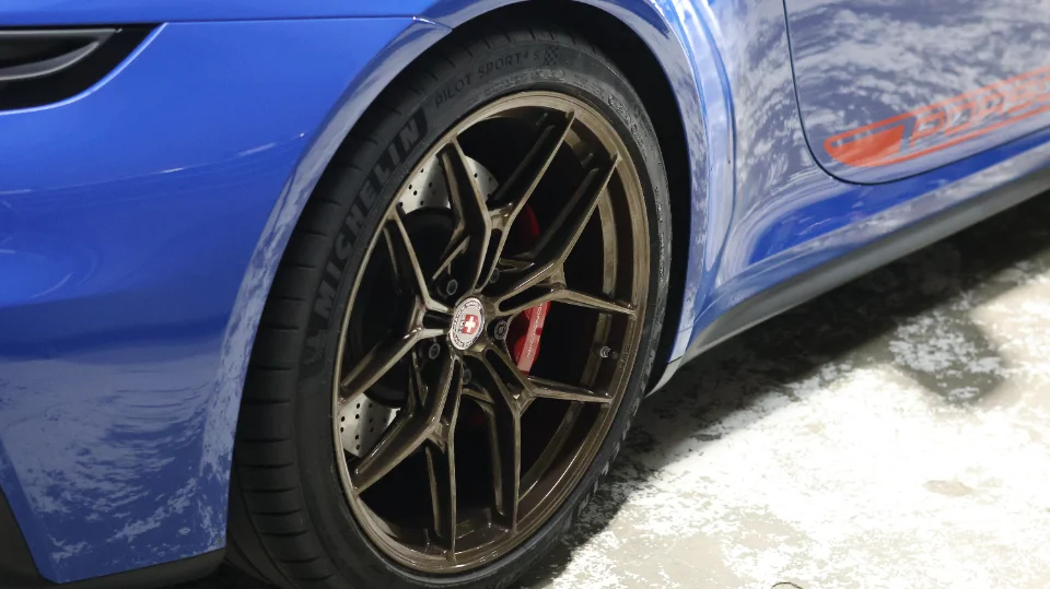 Close-up of a blue Porsche with bronze HRE wheels, Michelin Pilot Sport 4S tires, and red brake calipers.