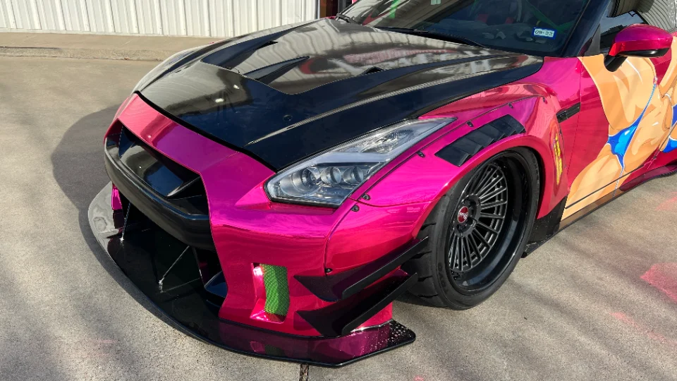 Custom widebody Nissan GT-R with a pink chrome wrap, carbon fiber hood, and aftermarket wheels parked outdoors.