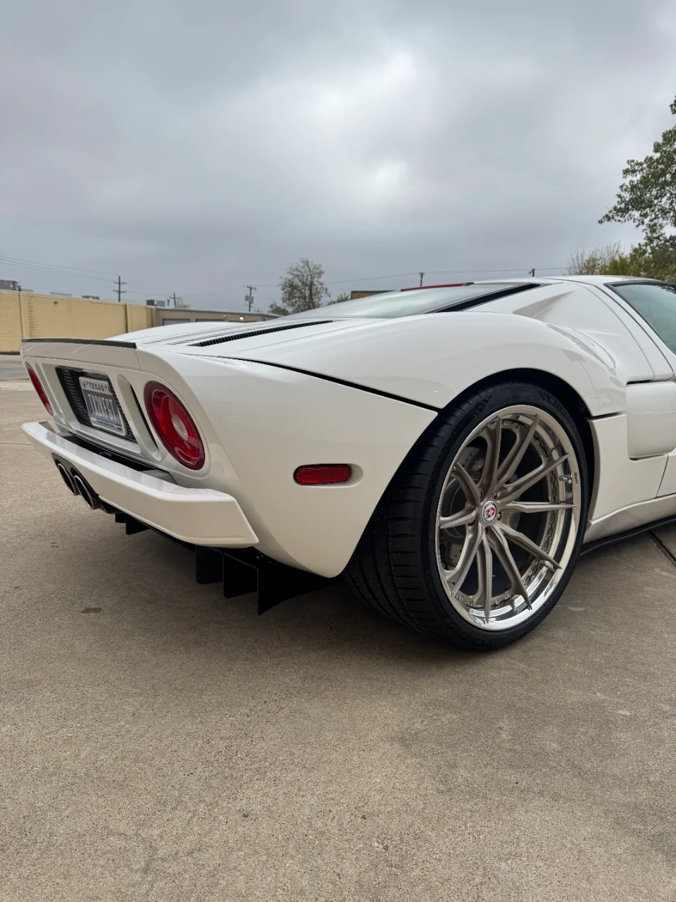 Rear view of a white Ford GT with custom wheels and a prominent rear diffuser parked on concrete.