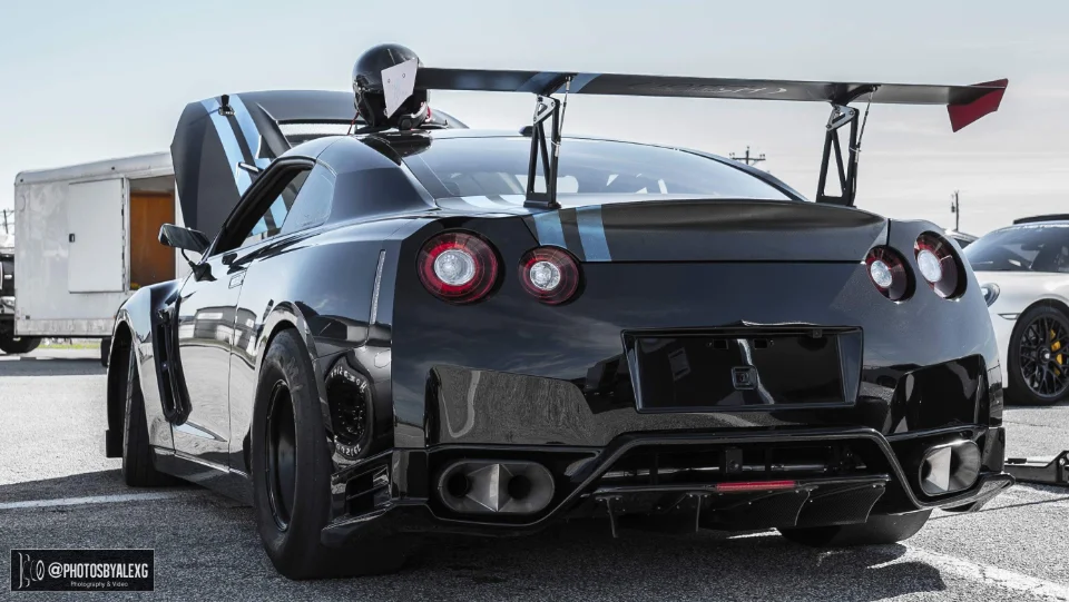 Rear view of a black Nissan GT-R drag car with a large aftermarket rear wing and drag tires at the track.