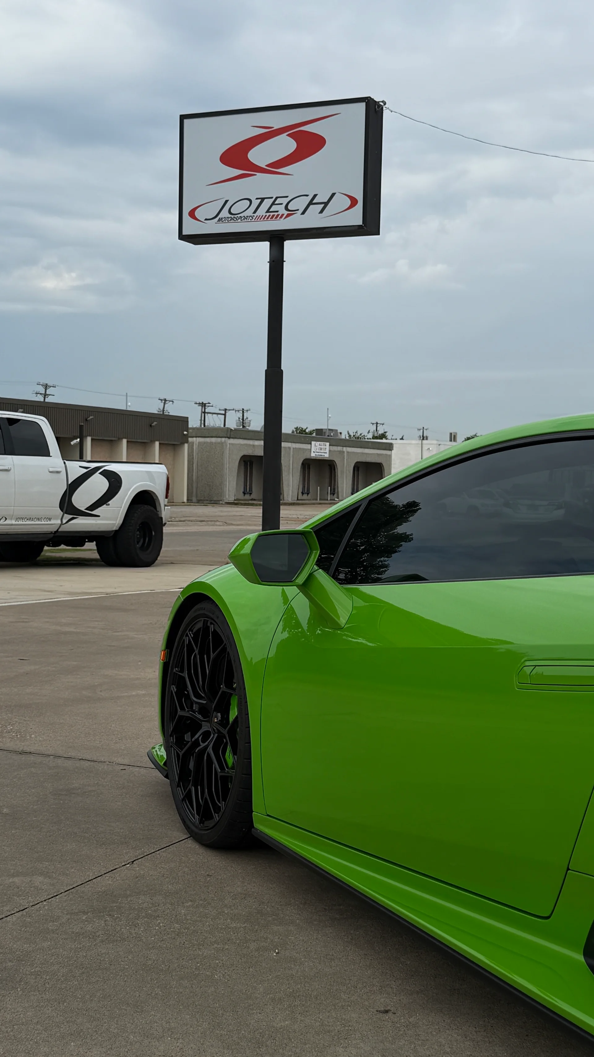 A bright green Lamborghini Huracan parked outside Jotech Motorsports facility with the shop's sign visible.